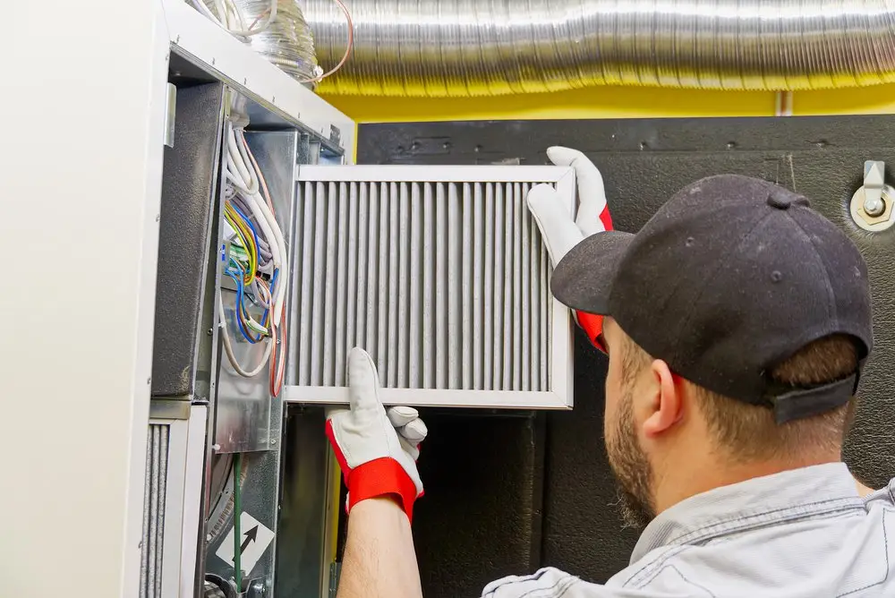 Technician installing a filter into an HVAC system or air conditioning unit, wearing protective gloves and a cap.