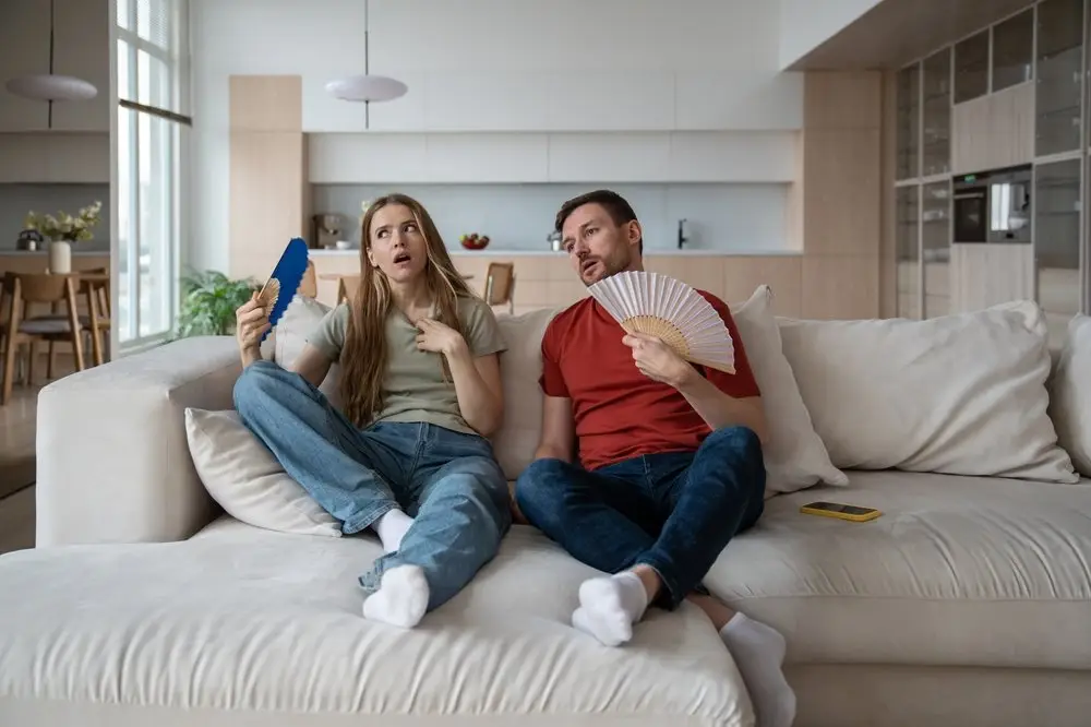 Couple on sofa fanning air because ac not working in the hot summer.