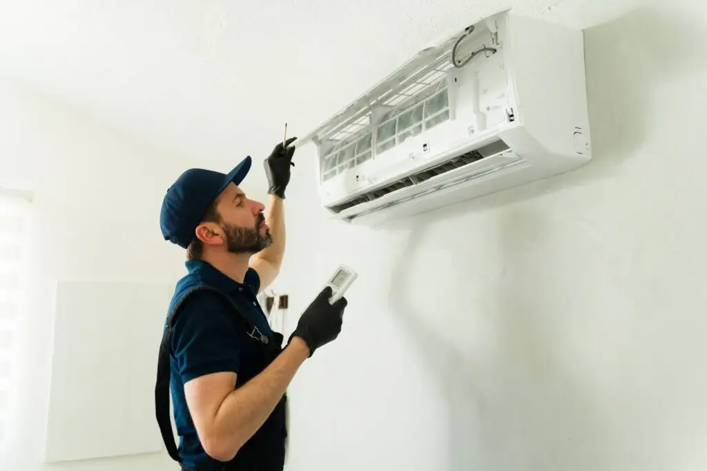 A technician cleaning a wall-mounted air conditioner unit with a small tool.