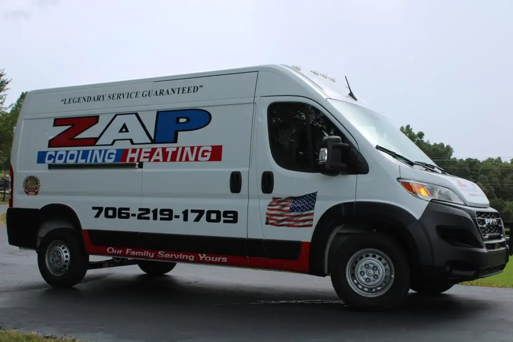 White service van with ZAP Heating and Cooling branding, American flag decal, phone number, and slogan, parked on a driveway with trees in the background.