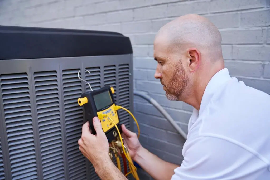 A technician inspecting an air conditioning unit with a digital multimeter outside a building.