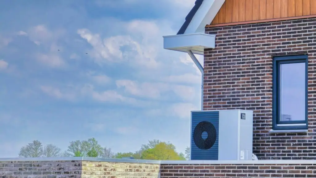 Close-up of the exterior of a brick building with an air conditioning unit and a window, under a partly cloudy sky.